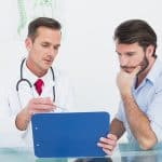 Male doctor discussing reports with patient at desk in medical o
