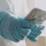 человек в медицинском халате и перчатках пересчитывает купюры