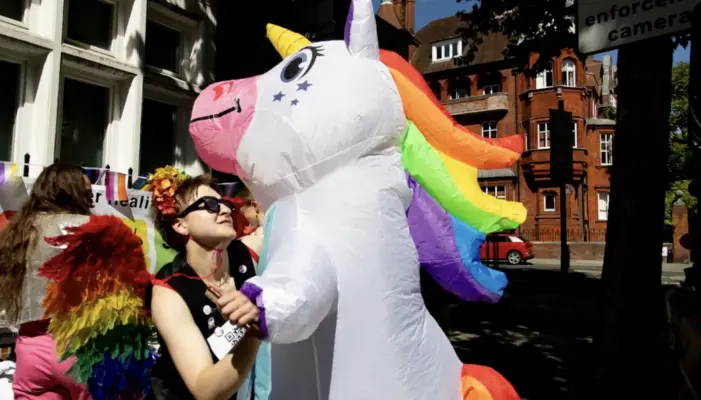 Женщина танцует с аниматором в костюме единорога с радужной гривой