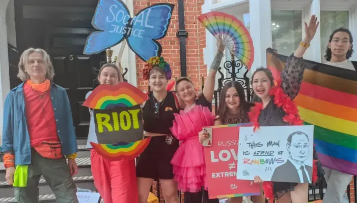 Акция Ясной Британии: квир-люди стоят с флагами и протестными плакатами напротив посольства России в Лондоне