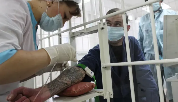 медсестра ерез решётку берёт кровь у заключённого