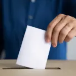 человек опускает лист в урну для голосования