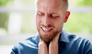 молодой мужчина с выражением боли держится руками за горло