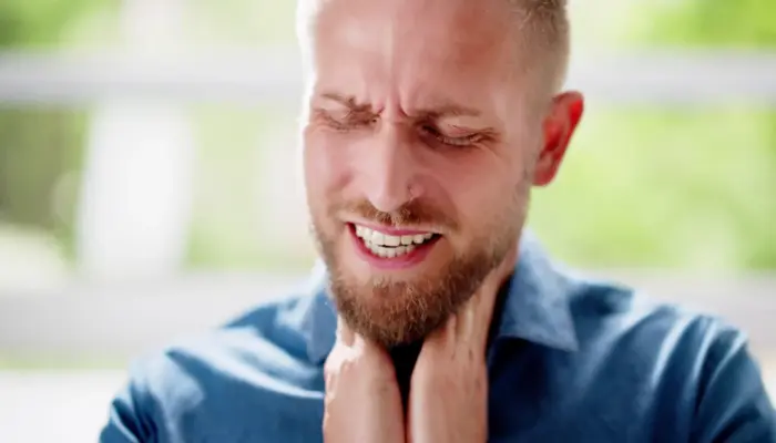 молодой мужчина с выражением боли держится руками за горло