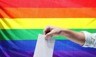 Рука опускает лист в урну на фоне радужного флага. ЛГБТ, голосование, выборы