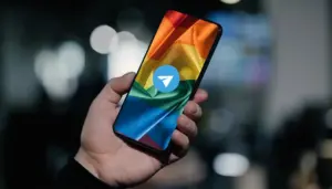 Рука держит телефон, на котором изображён прайд-флаг и поверх него иконка Телеграма