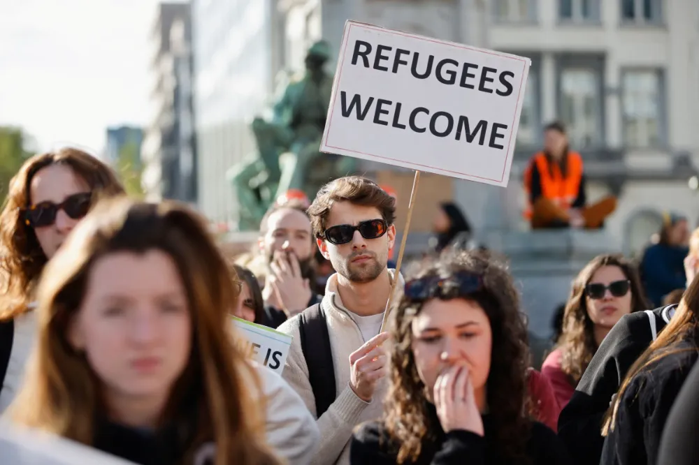 митинг, в центре кадра молодой человек с баннером "refugee are welcome"