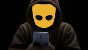 человек с логотипом Grindr вместо лица смотрит в телефон в темноте