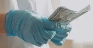 человек в медицинском халате и перчатках пересчитывает купюры