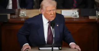 президент США Дональд Трамп выступает с трибуны с недовольным лицом
