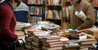 два человека рассматривают прилавок, заполненный книгами, на фоне книжных полок